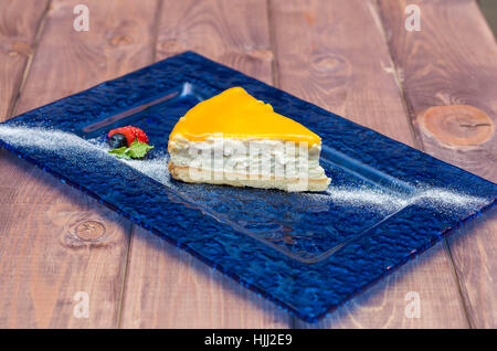 cheesecake with mango sauce, passion fruit on a blue background with powdered sugar and a strawberry Stock Photo