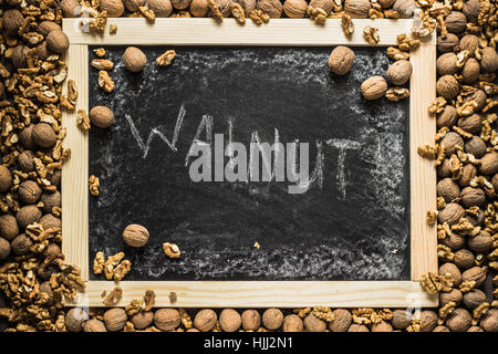 Whole and open ripe walnuts frame around black chalkboard with "walnut" inscription in the center. Photograph taken from above, top view. Stock Photo