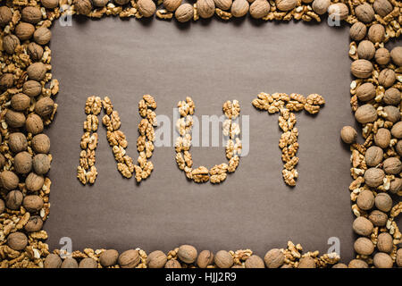 The word 'nut' is written from the walnuts on a dark brown paper background in a frame of walnuts. View from above Stock Photo