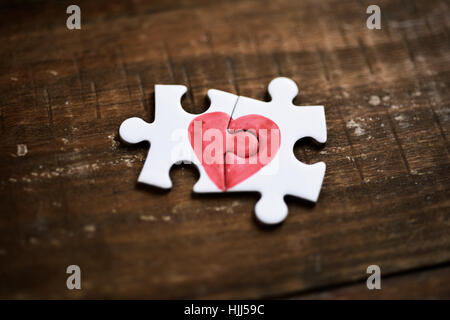 closeup of two pieces of a puzzle forming a heart on a rustic wooden surface, depicting the idea of that love is a thing of two Stock Photo