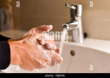 closeup of a young caucasian man washing his hands with soap in the sink of a bathroom Stock Photo
