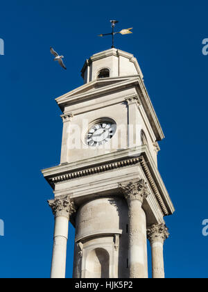 The newly cleaned and refurbished Herne Bay clock tower, in Kent, Uk with a seagull flying by on a summer day with a blue sky . Stock Photo
