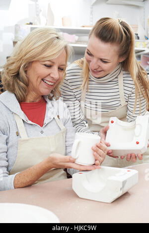Teacher With Mature Woman Making Mug In Pottery Class Stock Photo