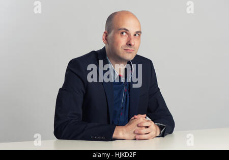 bald man sits at the desk and looking up Stock Photo