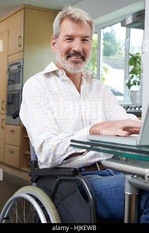 Disabled Man In Wheelchair Using Laptop At Home Stock Photo