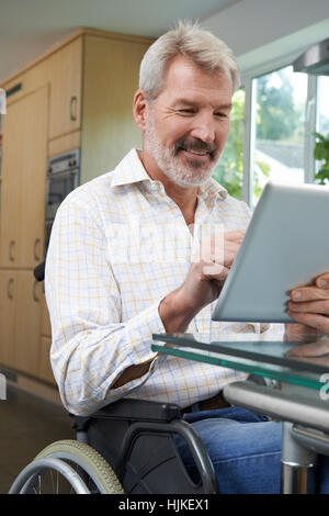 Disabled Man In Wheelchair Using Digital Tablet At Home Stock Photo