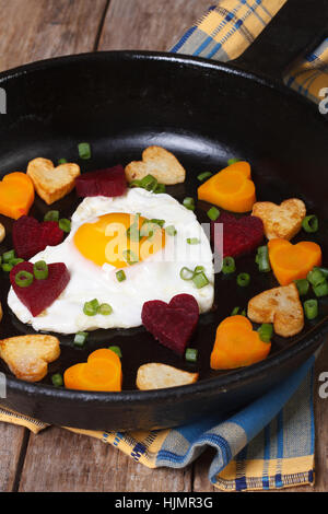 Egg in the form of heart in a pan with vegetables closeup. vertical Stock Photo