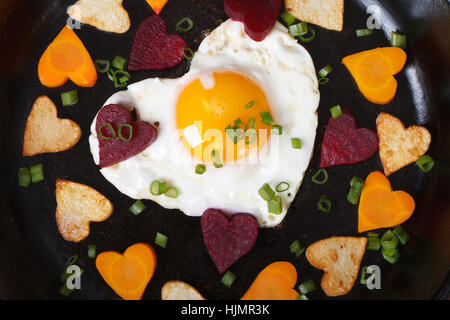 Hearts of carrots, potatoes, beets and eggs in a frying pan macro. top view Stock Photo
