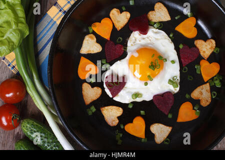 Romantic breakfast on Valentine's Day of fried eggs and vegetables in the shape of hearts closeup on a frying pan. top view Stock Photo