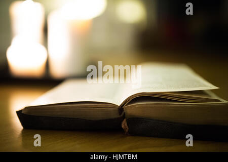 Bible laid on wooden floor, burning candles in the background Stock Photo