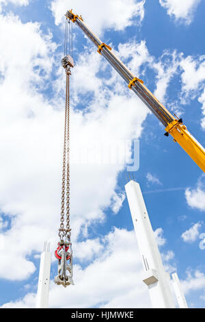 Construction crane with a hook and a metal profile hanging on ropes lifting  up, low angle view with cloudy sunny blue sky Stock Photo - Alamy
