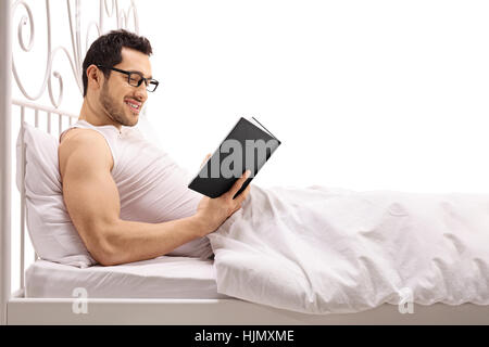 Man lying in bed and reading a book isolated on white background Stock Photo