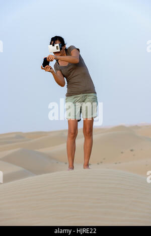 Woman (in the 40s) wearing a Virtual Reality headset (VR mask) and playing in the desert. Stock Photo
