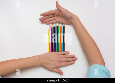 On a sheet of paper lie pencils Female hands lie above and below them Stock Photo