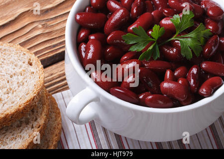 cooked red kidney beans in a white bowl and sliced bread closeup on a wooden table. horizontal top view Stock Photo