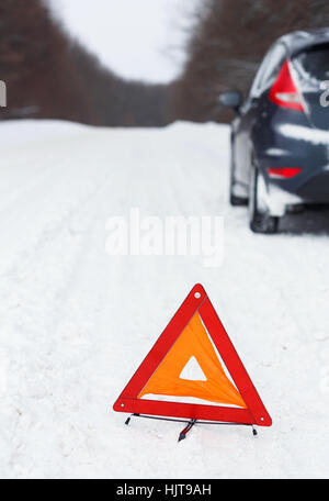 Transportation, winter and vehicle concept - closeup of red warning triangle with a broken down car Stock Photo
