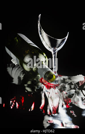Broken wine glass with bottle and foil, on black background with cherry and reflections.  Photographed in-studio on reflective mat. Stock Photo