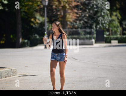 Young girl drinking water while walking down the street, wearing jean shorts and black t-shirt Stock Photo