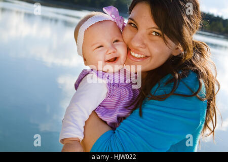 Mom holding smiling baby girl by a lake Stock Photo