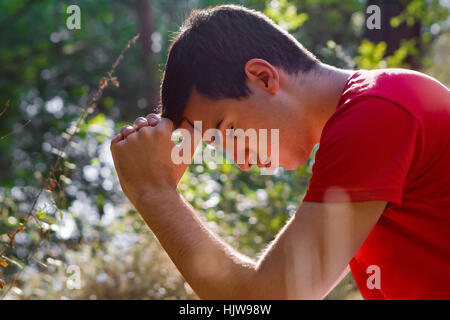 Young man kneeling and praying in forest Stock Photo