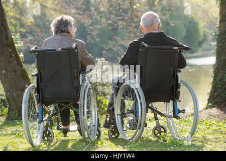 Elderly couple in wheelchairs, looking at view Stock Photo