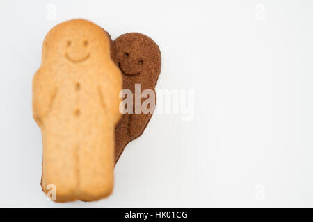 A cheeky black gingerbread man peeking over the shoulder of a white gingerbread man and having fun on a white background. Stock Photo