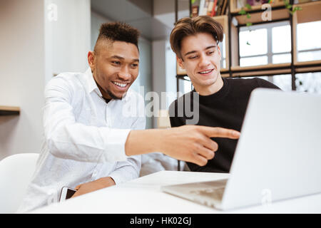 Photo of two young students sitting in library and using laptop computer. Look at laptop. Stock Photo