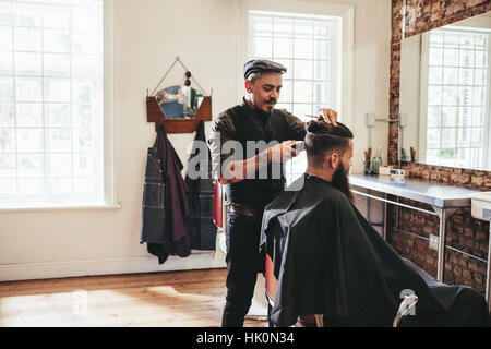Male barber giving client haircut in shop. Hairdresser styling hair of client at salon. Stock Photo