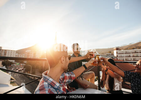 Friends toasting drinks at a party. Young friends hanging out at rooftop party and enjoying drinks. Stock Photo