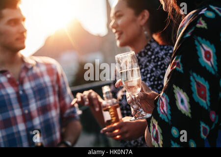 Champagne glass in hand of a women standing with friends at party. People having drinks at party. Stock Photo