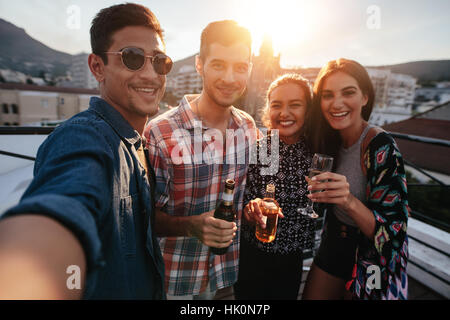 Young friends partying together taking selfie. Group of people with drinks on a rooftop party taking selfie. Stock Photo