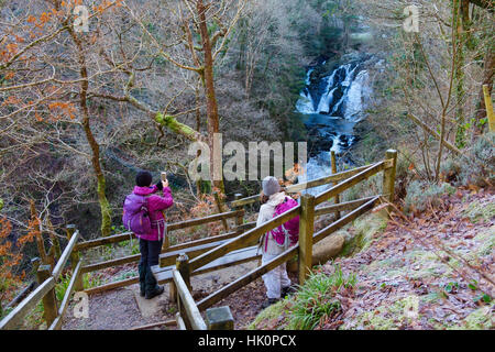 Hikers with an smartphone photographing Swallow Falls on Afon Llugwy River in Snowdonia from viewpoint on northern side. Betws-y-Coed Conwy Wales UK Stock Photo