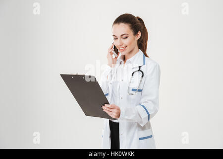 Cheerful attractive young woman holding clipboard and talking on mobile phone over white background Stock Photo