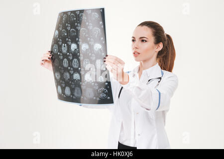 Concentrated young woman doctor standing and looking at x-ray picture over white background Stock Photo