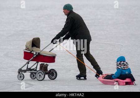 Steinebach, Germany. 25th Jan, 2017. An ice-skater glides across the frozen Woerthsee lake pushing a stroller and pulling his daughter on a sled near Steinebach, Germany, 25 January 2017. Photo: Peter Kneffel/dpa/Alamy Live News Stock Photo