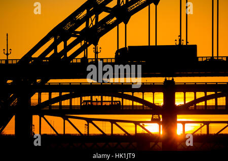 Newcastle upon Tyne, England, United Kingdom. View down the river Tyne from the Quayside as the sun sets behind the famous Tyne Bridge, the High Level Bridge and the Metro Bridge. Stock Photo