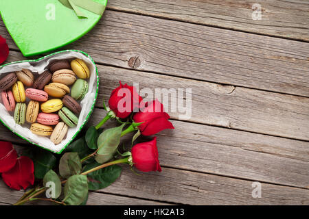 Valentines day greeting card. Red roses and macaroons gift box on wooden table. Top view with space for your greetings Stock Photo
