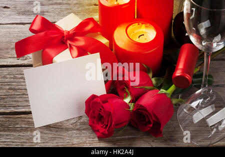 Valentines day greeting card. Red rose flowers, wine, gift box and candles on wooden table. With space for your greetings Stock Photo