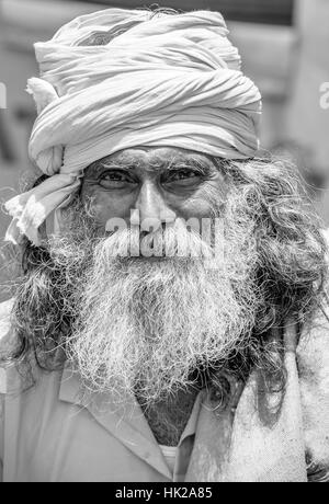 Close-up portrait of an elderly Indian man (Sadhu) in a vibrant orange outfit, capturing his wise expression, vertical black and white headshot Stock Photo