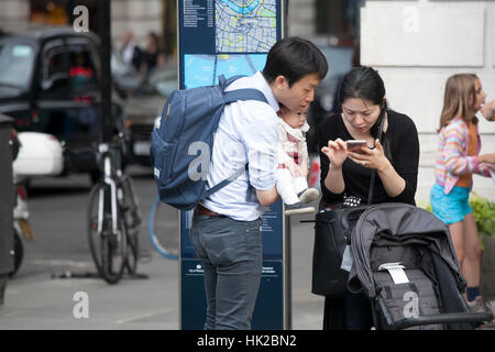 LONDON, ENGLAND - JULY 12, 2016 Family of tourists: father, mother and baby in her arms - looking in the phone, trying to determine the route Stock Photo