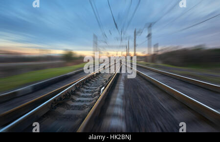 Railroad in motion at sunset. Railway station with motion blur effect against blue sky, Industrial concept background Stock Photo