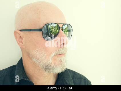 Old man with cool sunglasses looking away. Green garden reflected in the glasses. Stock Photo