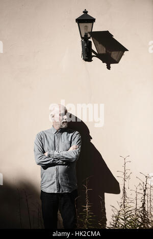 Serious and cool old man standing in front of wall. Sunshine and heavy shadow. Building exterior with copy space. Stock Photo