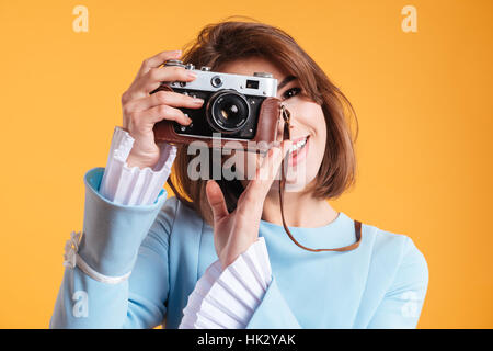 Portrait of smiling young woman taking photos with old vintage camera over yellow background Stock Photo