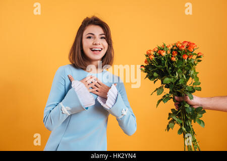 Cheerful excited young woman smiling and receiving bouquet of flowers over yellow background Stock Photo