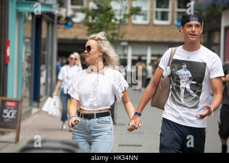 LONDON, ENGLAND - JULY 12, 2016 Happy couple in the white T-shirts, holding hands, walking on the street Stock Photo