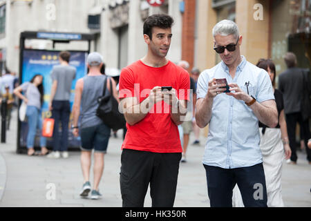 LONDON, UK - August 27, 2016: Composite image of two friends standing to the side slightly sending texts Stock Photo
