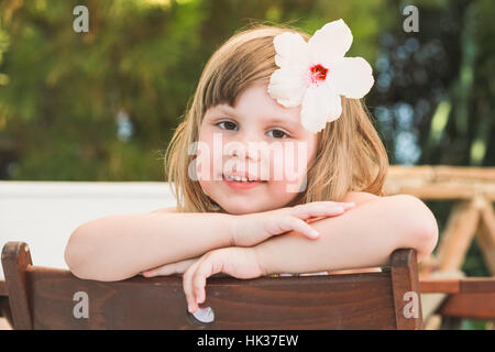 Cute smiling Caucasian little girl with white flower in hair, close-up outdoor portrait Stock Photo