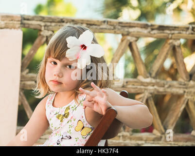 Serious Caucasian little girl with white flower in hair, outdoor portrait Stock Photo