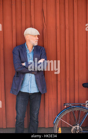 Old man and bike in front of red wall. Portrait of elderly person with healthy lifestyle. Stock Photo